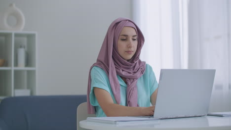 Mujer-Musulmana-Trabajando-En-Una-Computadora-Portátil-En-La-Oficina-Con-Sus-Compañeros-De-Trabajo-Cristianos.-Retrato-De-Cerca-De-Una-Joven-Empresaria-Musulmana-Con-Hijab-Usando-El-Portátil-En-El-Interior-Del-Apartamento